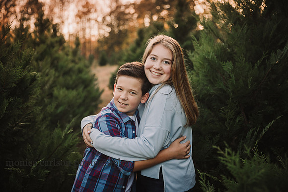 teenage siblings hug while standing among christmas trees at sunset