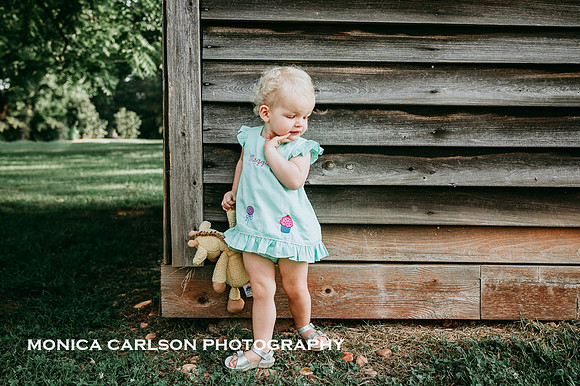 one year old girl posing in front of a historic wooden building