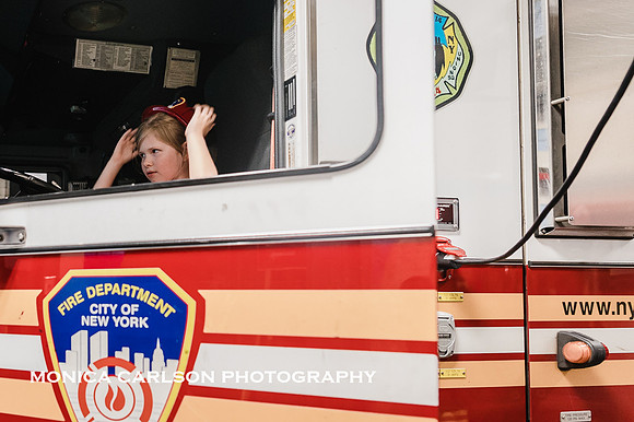 girl wearing a fire hat sits in a fire truck in New york city