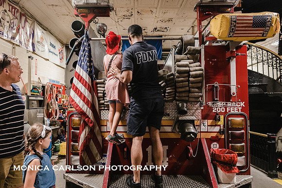 New york city fireman shows a little girl the hose in the back of the firetruck which is in a station house