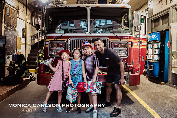 three kids pose with a new york city fireman in front of his fire house