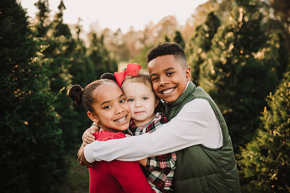 three mixed race sibling snuggling while standing on a Christmas Tree farm in Cumming, GA