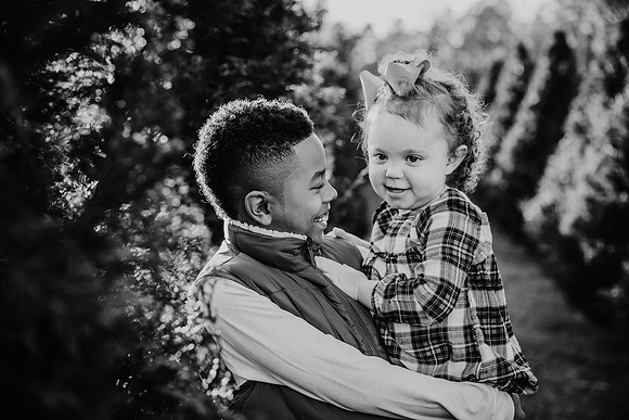 black and white image of a tween brother carrying his toddler sister by monica carlson