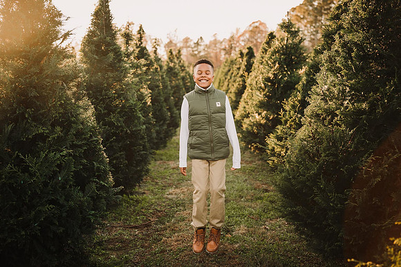 happy tween african american boy jumping up and down between rows of chritsmas trees.