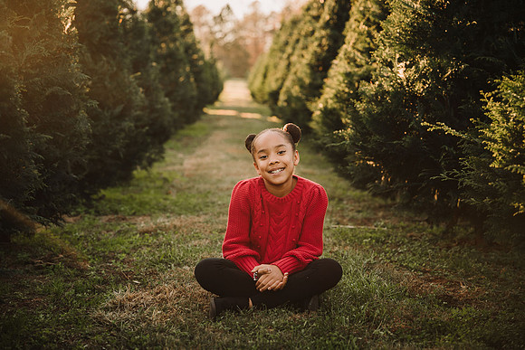 tween african american girls sitting indian style on the ground between two rows of christmas trees