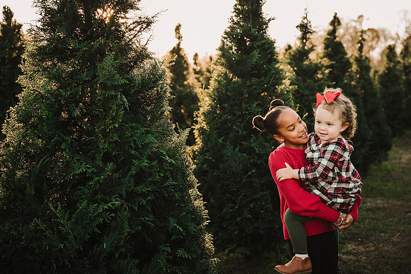 tween girl holding her toddler sister at a Christmas Tree farm by monica carlson