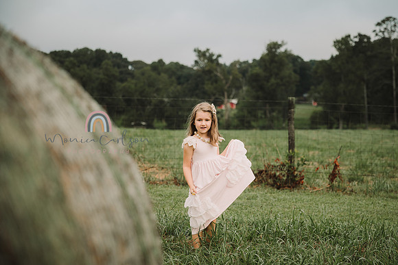 little girl looks passed a hay bale while holding her dress