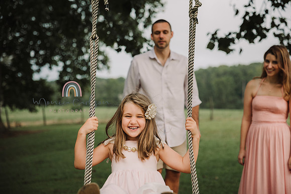 Father pushes his happy girl on a tree swing while mom looks on