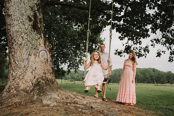 happy little girl is pushed by father on a tree swing while mom watches
