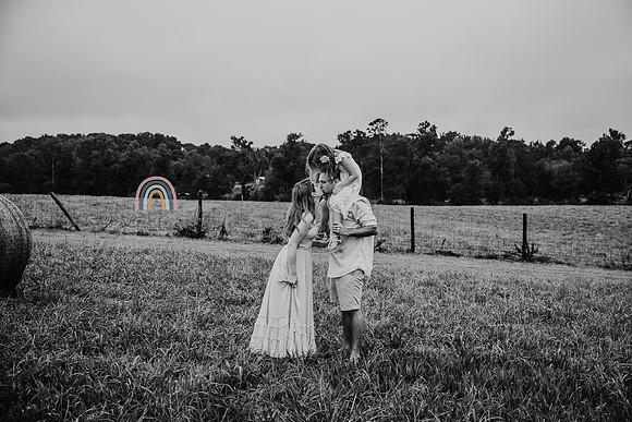 black and white image of parents kissing while their daughter sits on dads shoulders