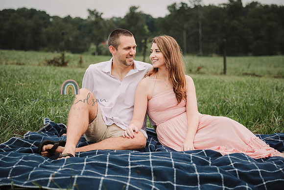 husband and wife sit on a blanket & look at each other lovingly