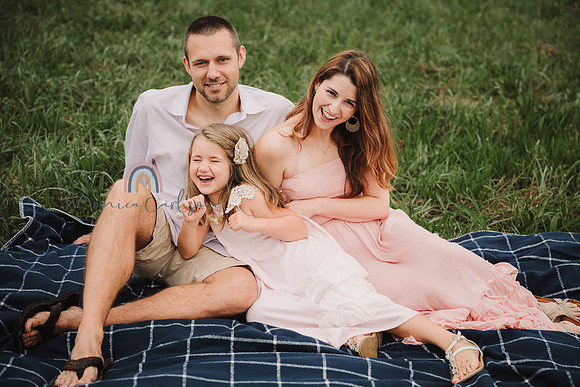mom, dad and daughter sit on a blanket and tickle wach other