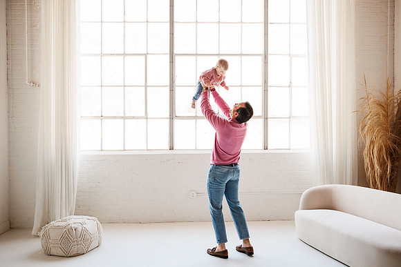 dad lifts his daughter in front a huge window in a King Plow studio