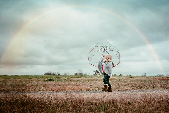 little girl walking down a path holding a umbrella under a rainbow