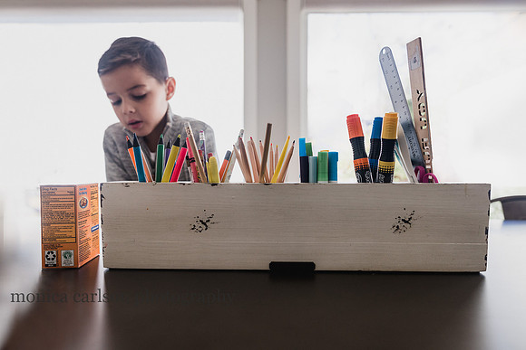 markers and pencils in a container with a boy in the background