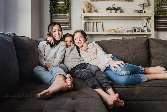 three siblings happily sitting in their living room together during a family photo session
