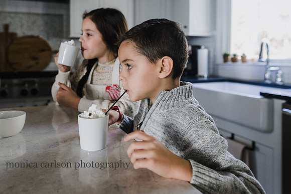 little boy drinking hot chocolate with his sister behind him