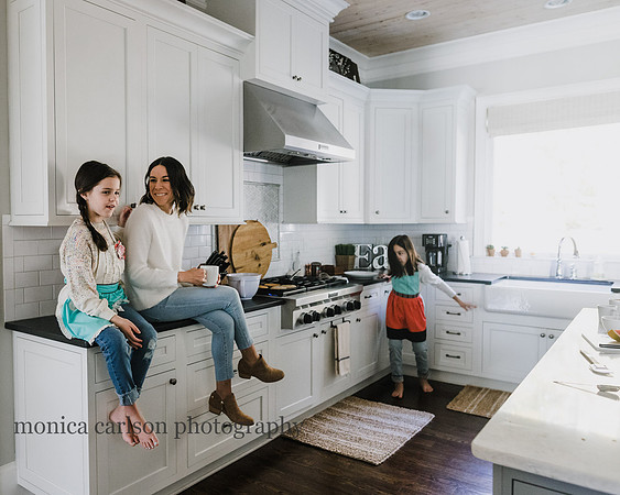 mother and daughter sitting on the kitchen counter while second daughter dances in the background