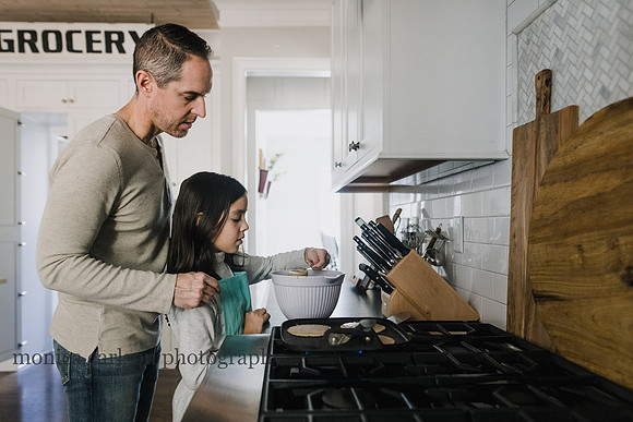 Father helping his daughter pour pancake batter onto a stove top