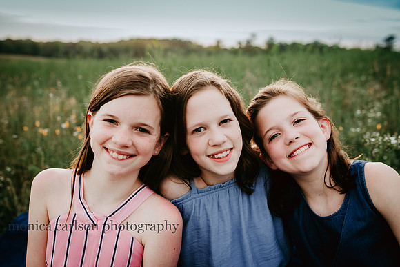 three preteen sisters smiling on a open field