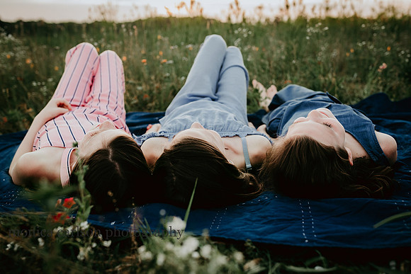 three sisters laying on a blanket in a field of flowers during a family photo session