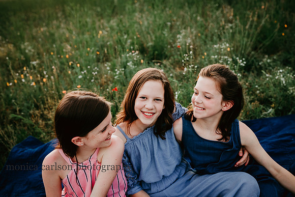 three girls talking while they sit on a blanket in a wild flower field at Prospect farms