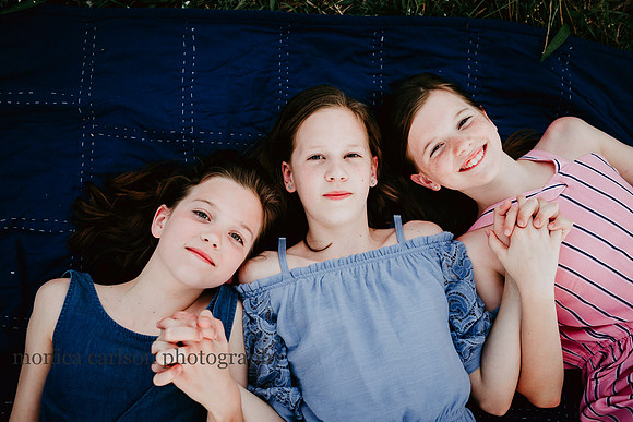 three sisters laying in a field, holding hand in prospect farms