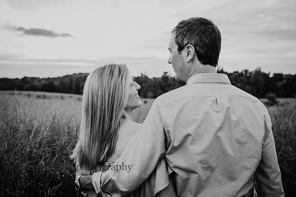 black and white portrait of a man and wife walking on a field &away from the camera