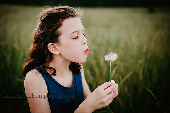 brown haired girl blowing dandelions