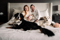 Newborn being held by her mom while sitting in a bed with dad and two dogs