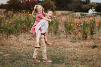 Little girl getting a piggie back ride from her brother in front of wild flowers