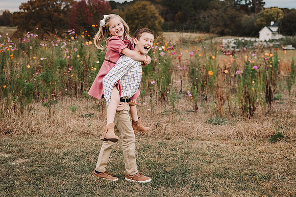 Little girl getting a piggie back ride from her brother in front of wild flowers