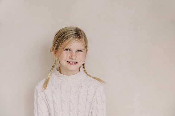 School Portrait of a smiling, blonde girl in front of a cream background