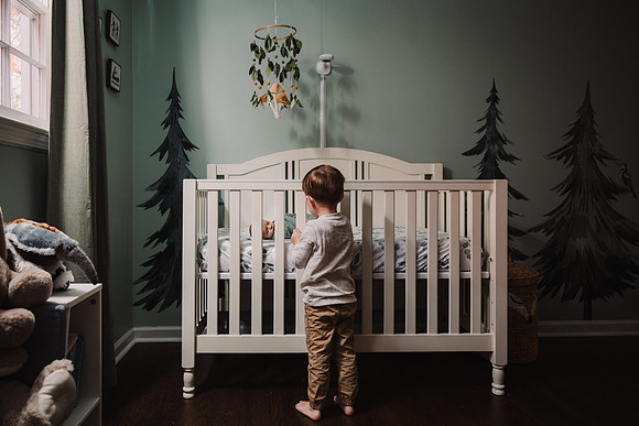 Little boy looks in to his newborn brothers crib