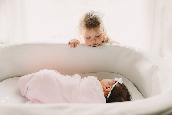 Toddler looks into her newborn sisters bassinet
