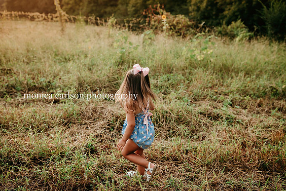 little girl walking through a field at sunset