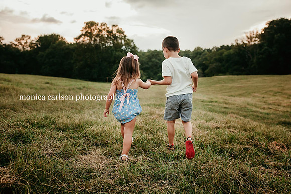 younger sister and brother holding hands has they walk on a field at a farm in cumming, ga