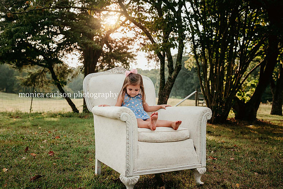 little girl sitting on a big chair under a tree at sunset