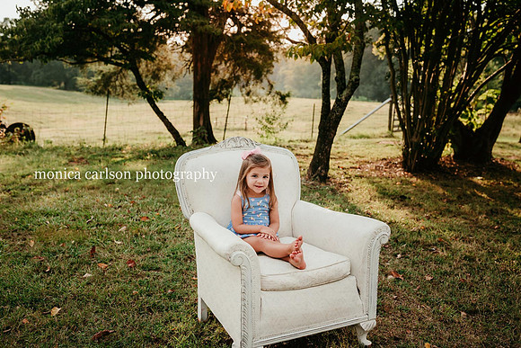 sweet smiling little girl sitting on a big white chair on a farm in cumming, ga