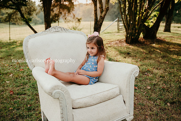 portrait of a little girl kicking her bare feet up on a love seat during a photo session with monica carlson