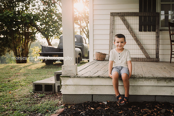 sweet little boy sitting on a wooden porch at a farm in cumming