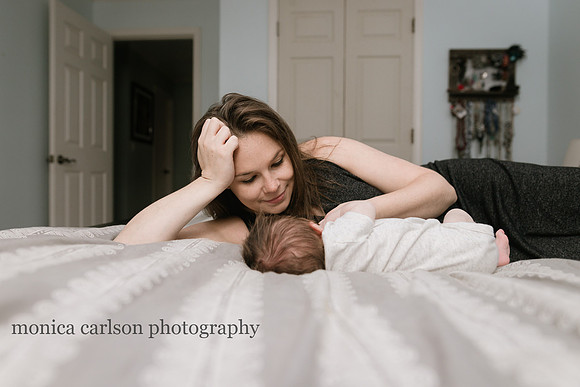 mother watches her baby sleep while laying on a bed in her home in atlanta