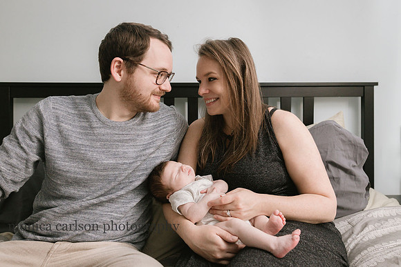 husband and wife looking at each other happily while caring for their new son during a home photo session