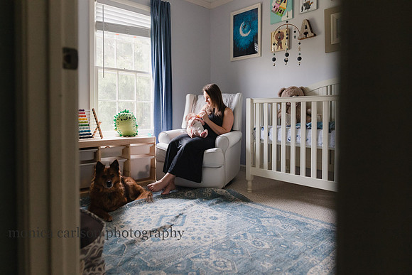 mother feeding her newborn baby boy with her dog by her feet during a photo session
