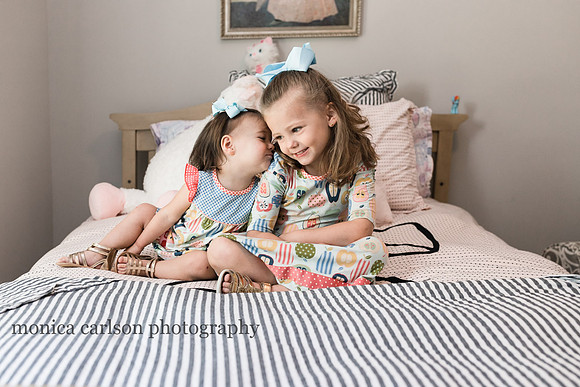 sweet sisters sitting on a bed and exchanging kisses by monica carlson