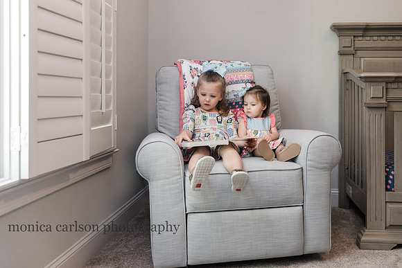 sisters sitting together in a chair reading a book in their room during a lifestyle photo session
