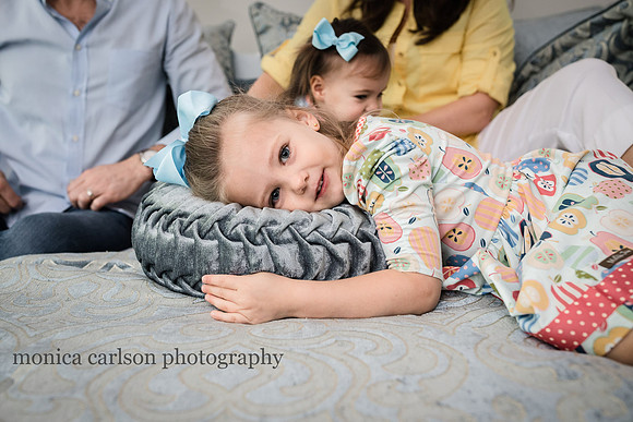 portrait of a tired little girl laying on a bed with her family in the background