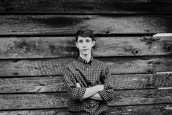 handsome teen boy leaning against a wooden barn by monica carlson