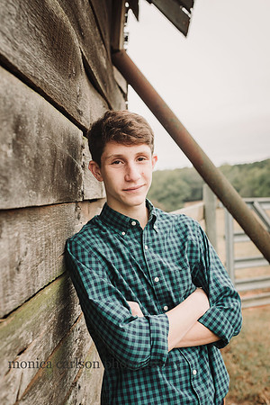 boy who is teen leaning against a wooden barn