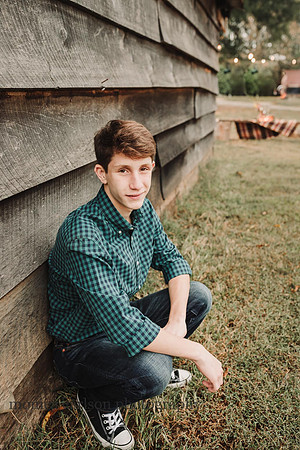 high school boy squatting against a barn during a family photo session